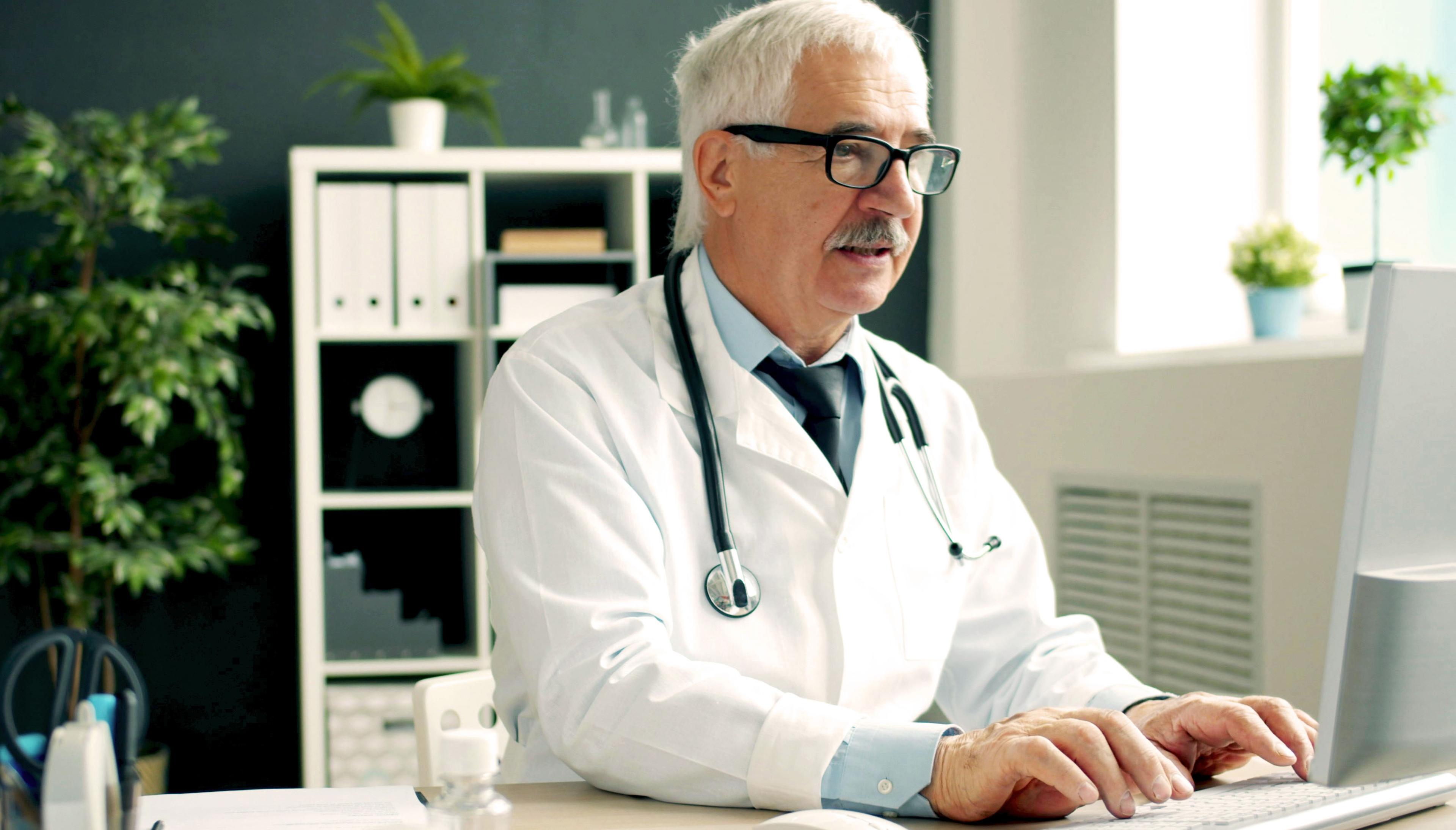 A doctor sitting at a desk typing on a computer in a medical office.