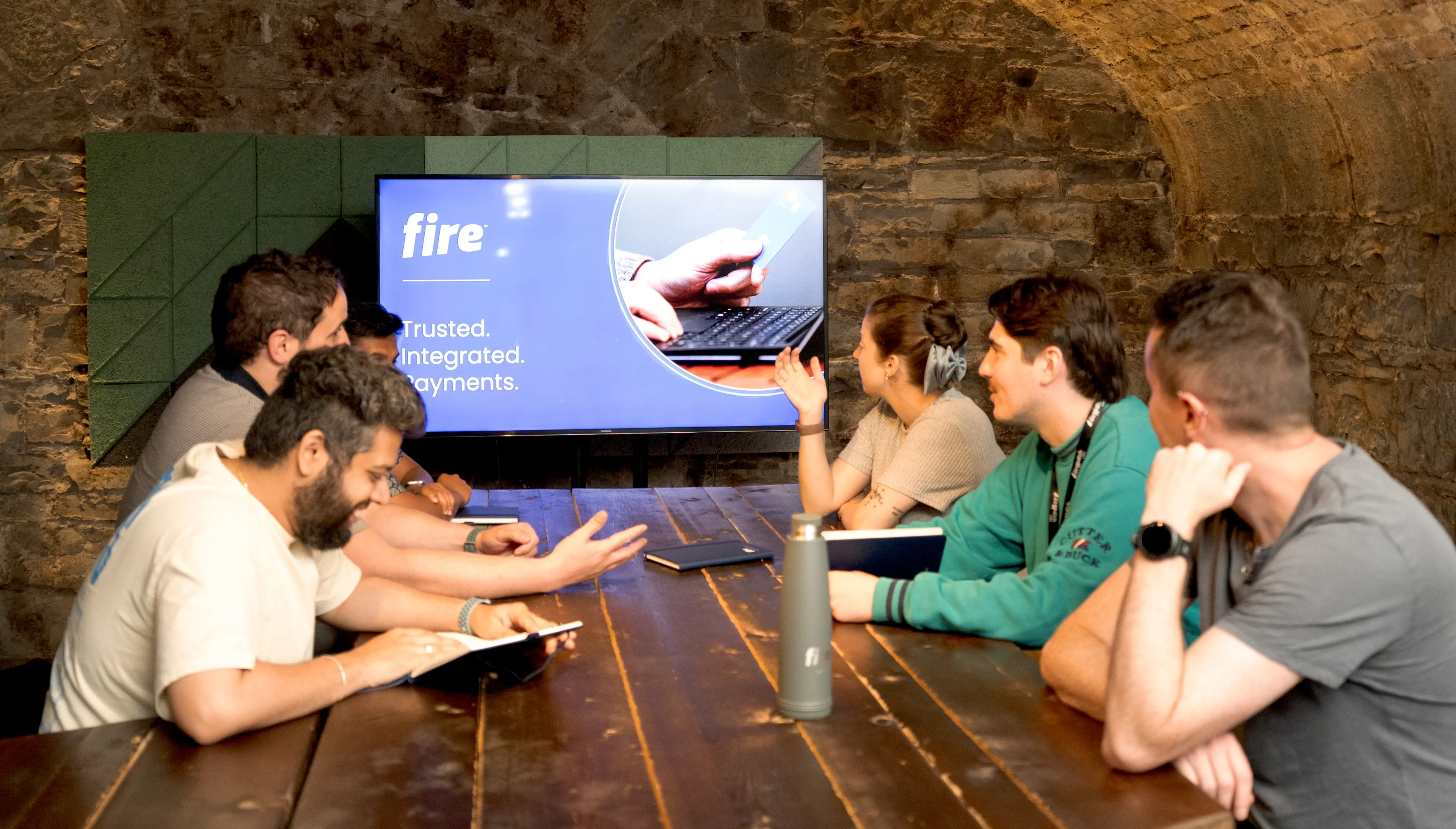A group of colleagues sitting around a table in a meeting room, looking at a screen displaying Fire branding.