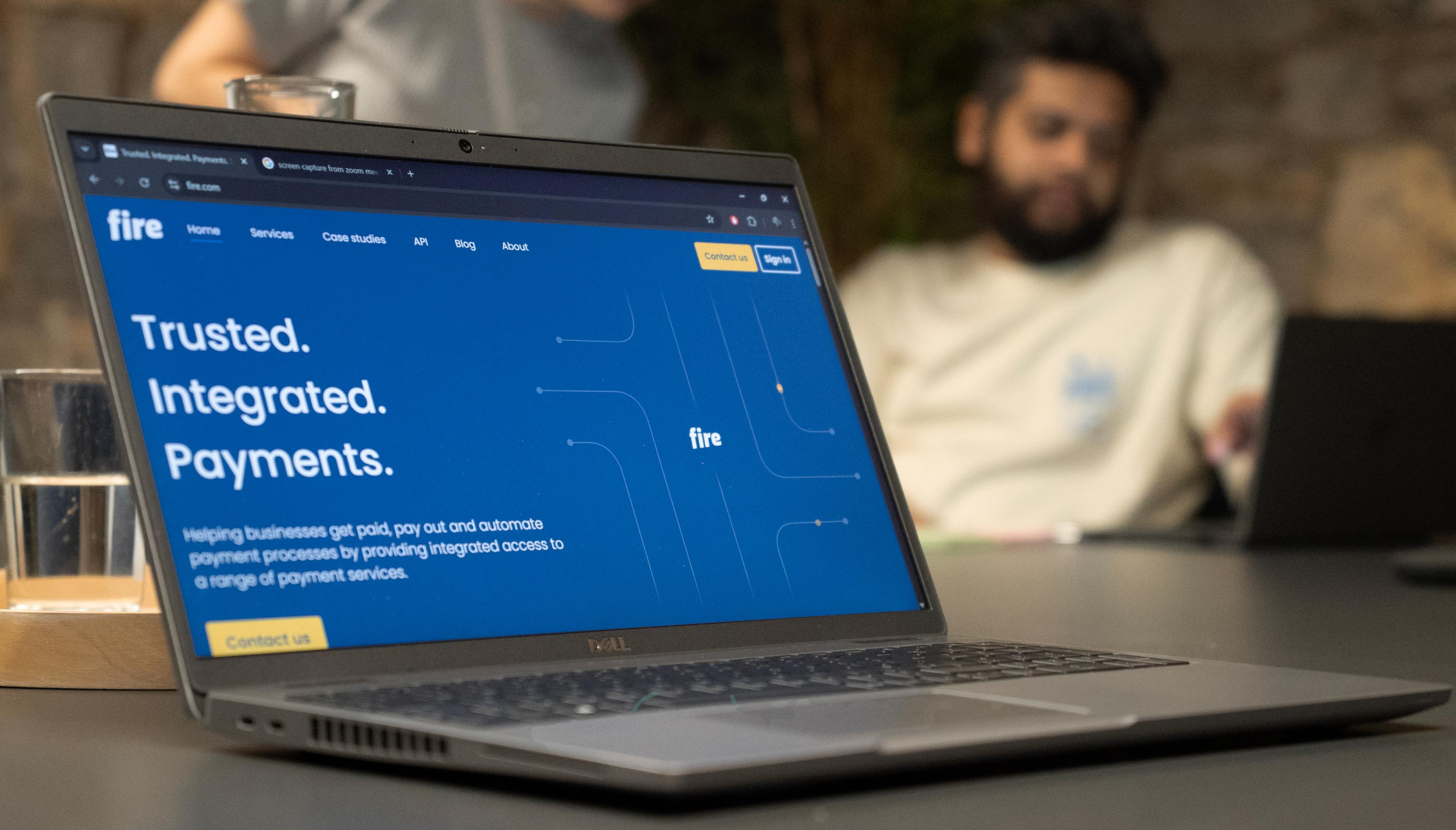 Laptop displaying Fire’s website on a meeting table, with two people working in the background.